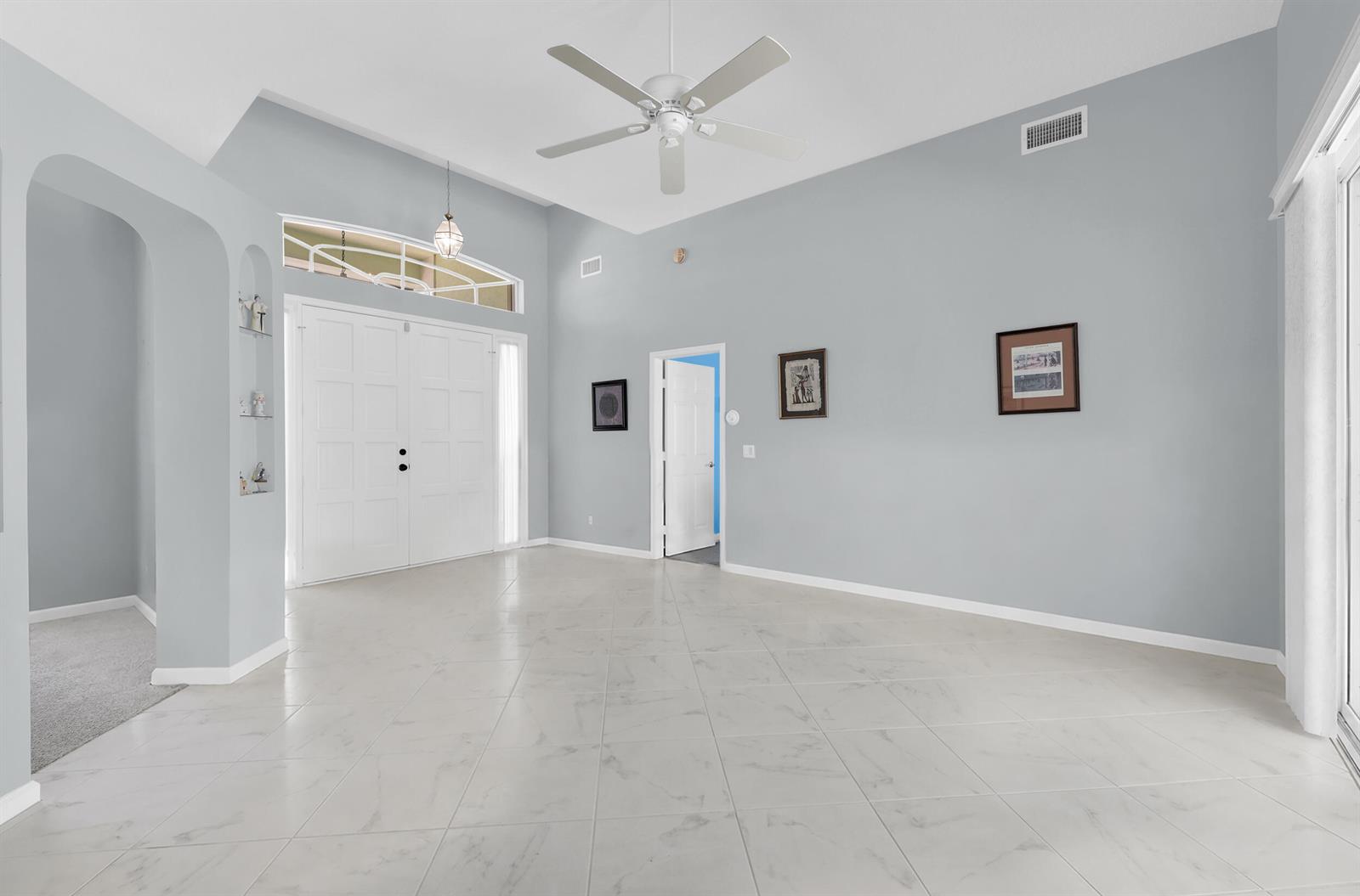 A spacious, light-gray living room with vaulted ceilings, white tile flooring, and double entry doors — 521 Cypress Circle, Tequesta FL 33469, TEQUESTA, FL