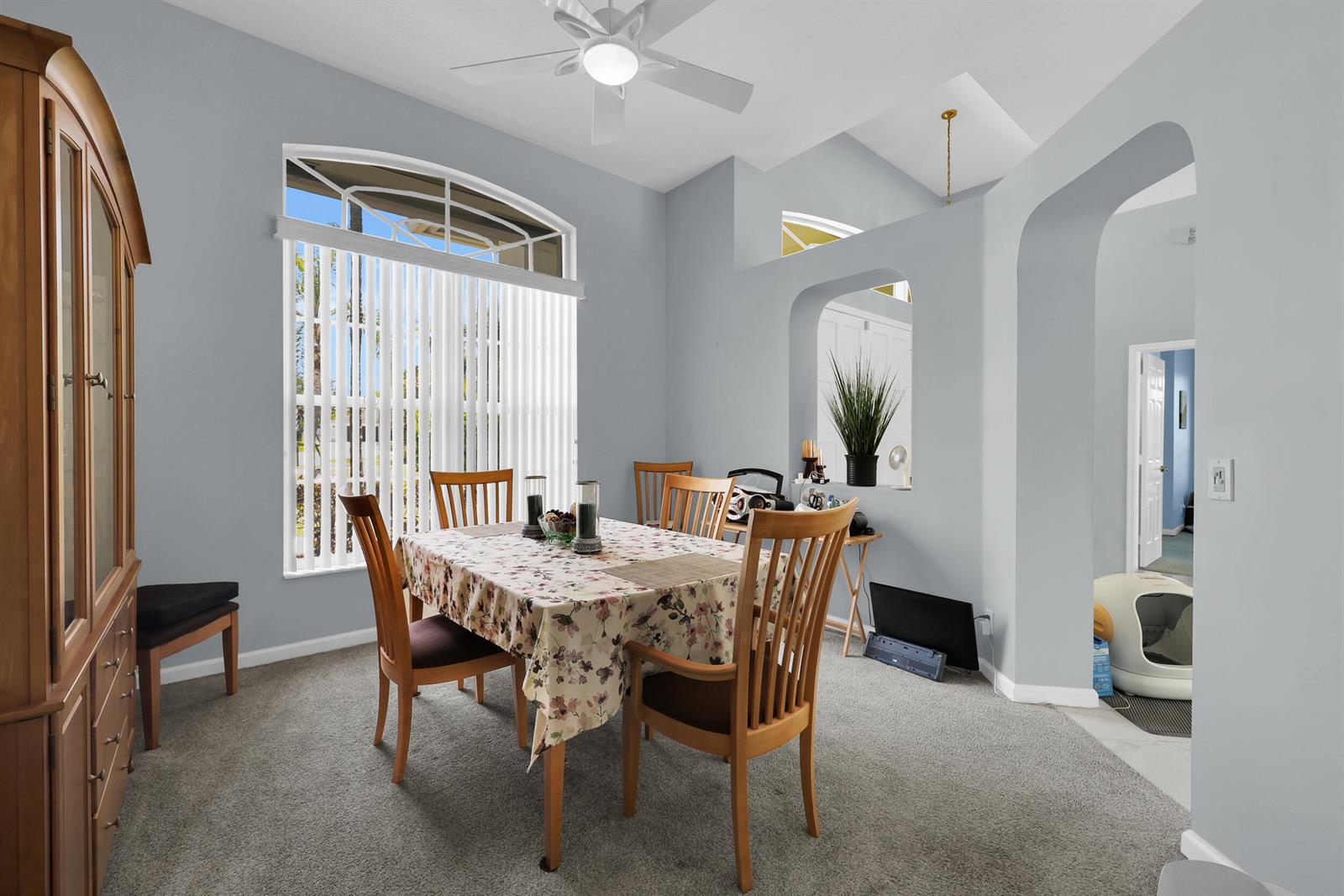 A dining room features a floral tablecloth, wooden chairs, carpeted flooring, and an arched window — 521 Cypress Circle, Tequesta FL 33469, TEQUESTA, FL
