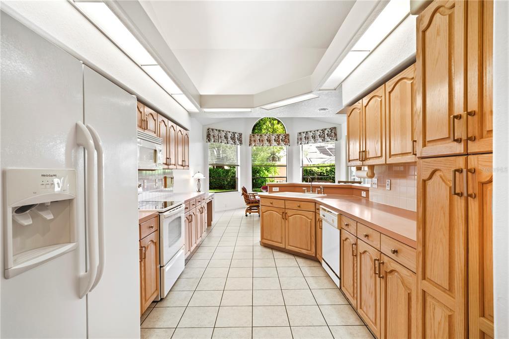 A kitchen features light wood cabinets, white appliances, tile flooring, and a large bay window — 9415 ASHLEY DRIVE, WEEKI WACHEE, FL
