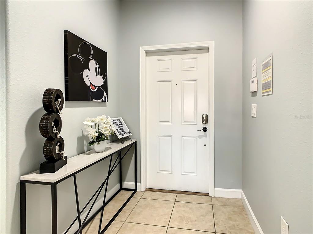 An entryway features a white door, a console table, Mickey Mouse art, and tile flooring — 8845 CANDY PALM ROAD, KISSIMMEE, FL