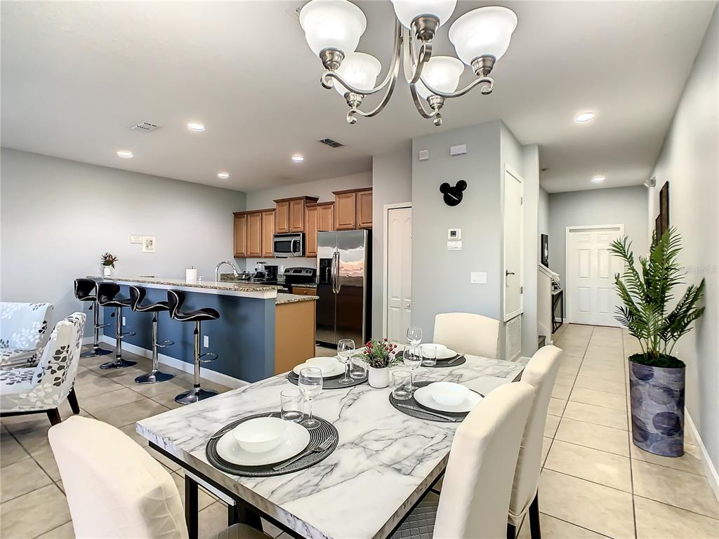 A dining area with a marble-topped table sits adjacent to a kitchen with bar seating — 8845 CANDY PALM ROAD, KISSIMMEE, FL