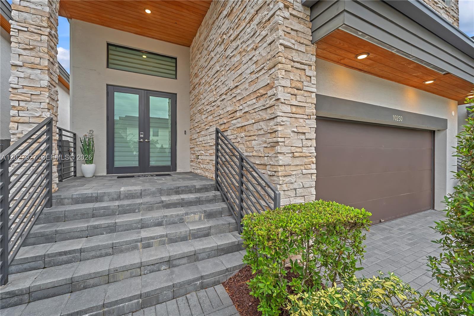 A stone-clad house exterior features a front entryway with gray steps and a garage — 10250 NW 76th Ter, Doral FL 33178, DORAL, FL