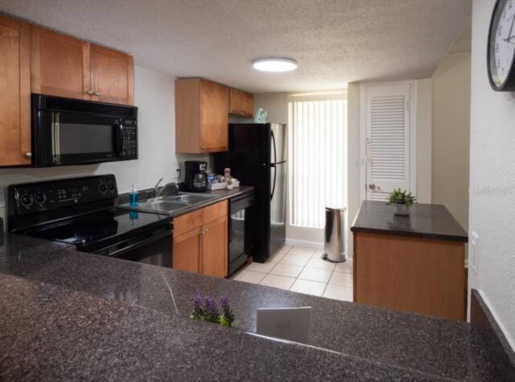 A kitchen with wood cabinets, black appliances, granite countertops, and a small island — 1810 NW 23RD BOULEVARD UNIT 178, GAINESVILLE, FL