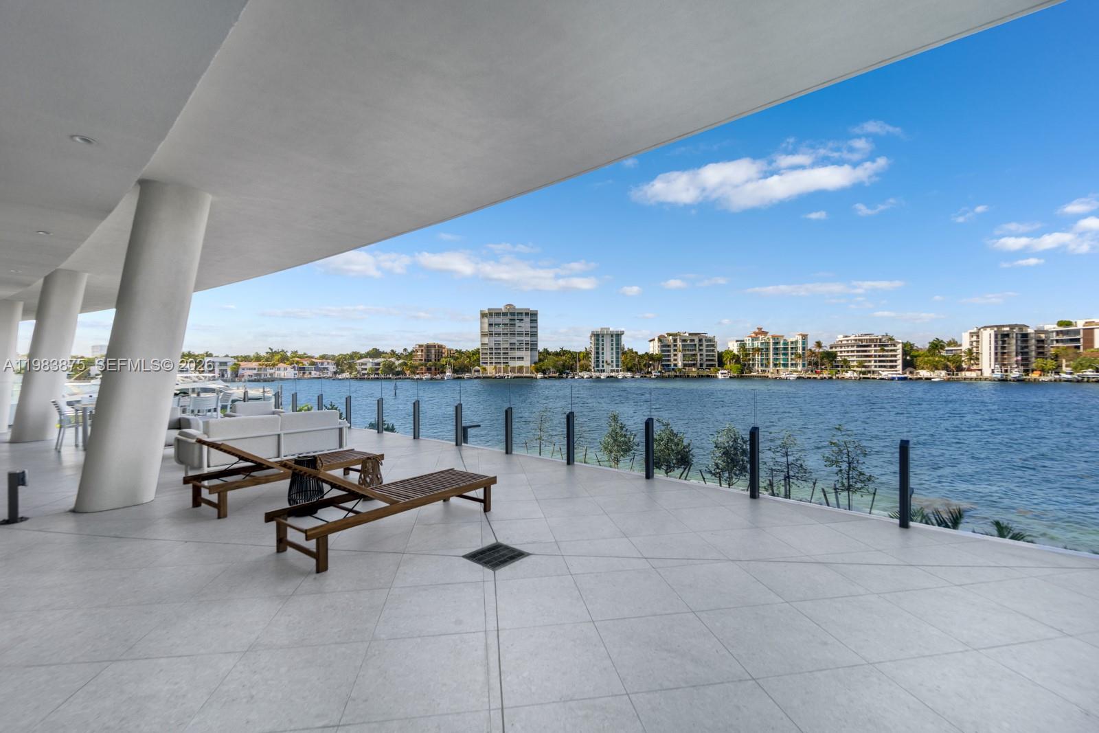 A spacious outdoor patio features lounge chairs, white columns, and a glass railing overlooking water — 5 Grove Isle Dr # L205, Miami FL 33133, MIAMI, FL