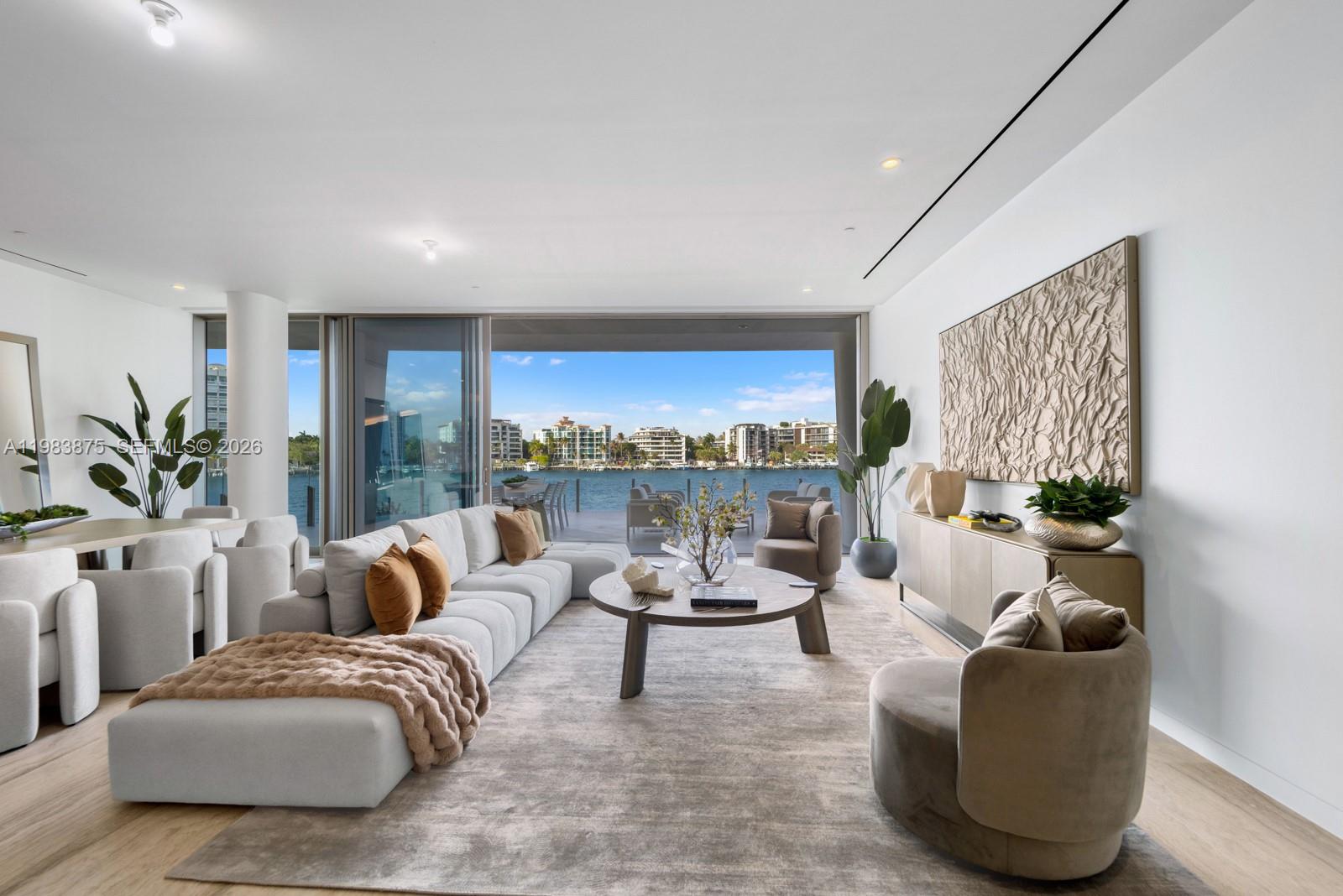 A modern living room features a large sectional sofa, circular coffee table, and waterfront views — 5 Grove Isle Dr # L205, Miami FL 33133, MIAMI, FL
