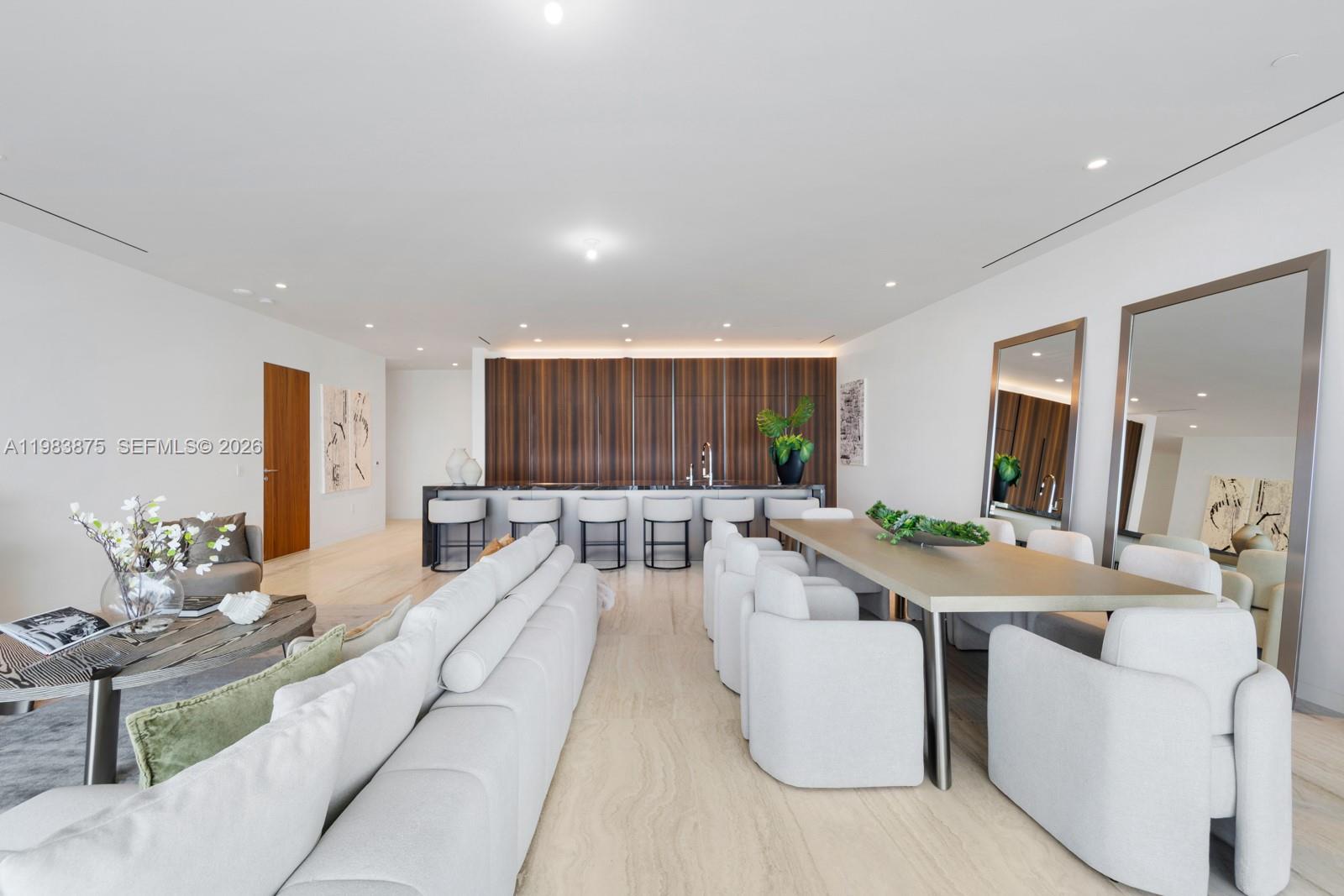 A modern open-concept living and dining area features white furniture, wood cabinetry, and stone flooring — 5 Grove Isle Dr # L205, Miami FL 33133, MIAMI, FL