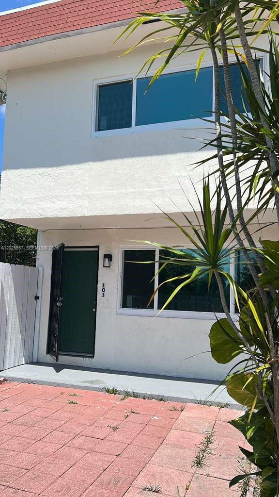 The exterior of a two-story white building features a dark green door and paved patio — 1450 NE 151st St # 101, Miami FL 33162, MIAMI, FL