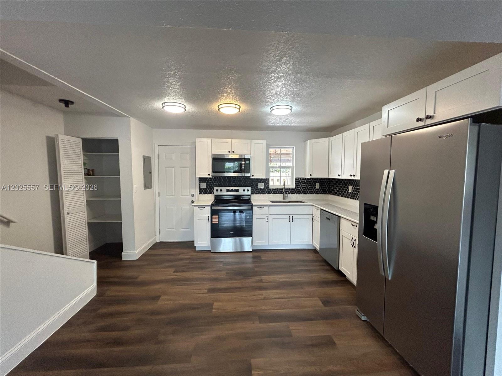 A kitchen features white cabinets, stainless steel appliances, a dark backsplash, and wood-look flooring — 1450 NE 151st St # 101, Miami FL 33162, MIAMI, FL