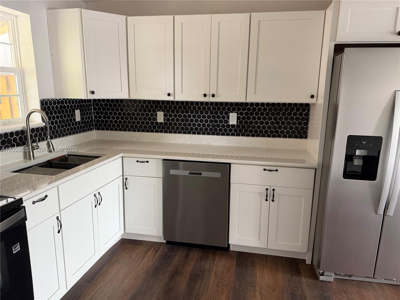 A kitchen features white cabinets, a black honeycomb tile backsplash, and stainless steel appliances — 1450 NE 151st St # 101, Miami FL 33162, MIAMI, FL