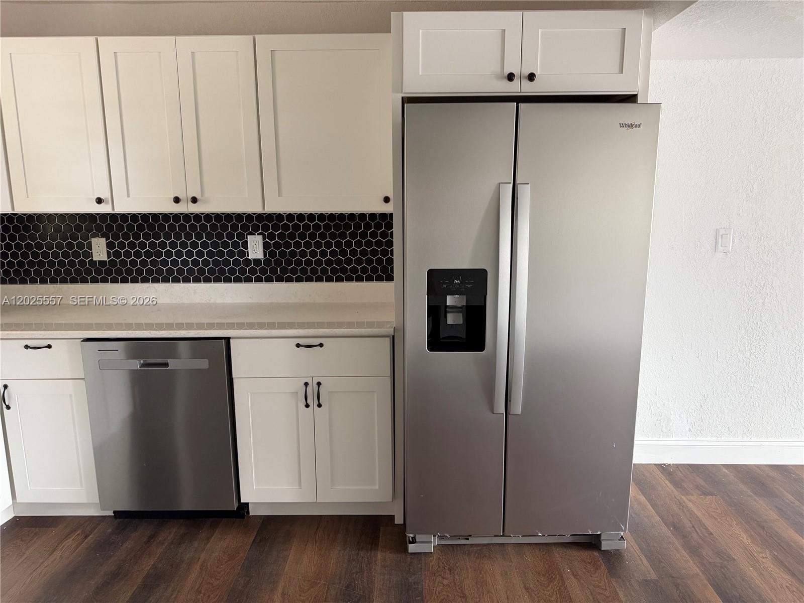 A kitchen features white cabinets, a stainless steel refrigerator and dishwasher, and black hexagonal backsplash — 1450 NE 151st St # 101, Miami FL 33162, MIAMI, FL