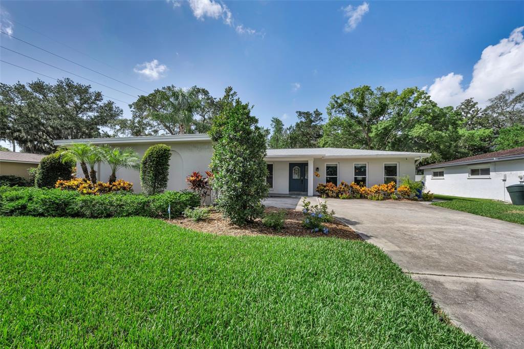A single-story house with a concrete driveway, manicured lawn, and landscaping under a blue sky — 1541 PLEASANT GROVE DRIVE, DUNEDIN, FL