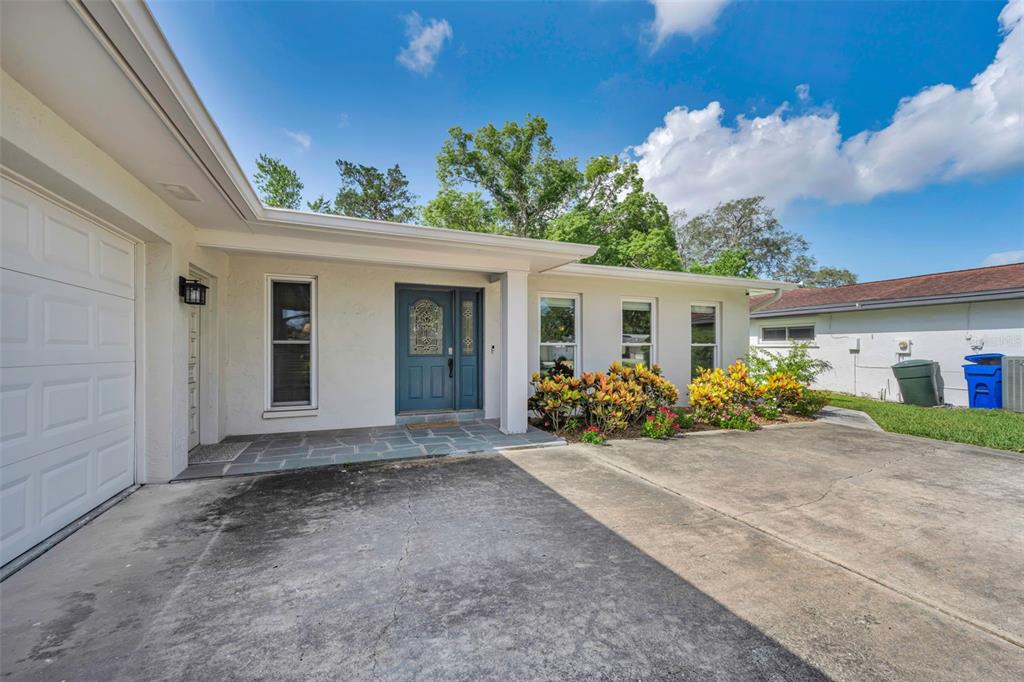 A single-story house exterior features a concrete driveway, a blue front door, and landscaping — 1541 PLEASANT GROVE DRIVE, DUNEDIN, FL