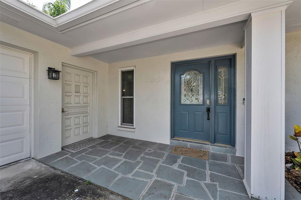 A covered entryway features a blue front door, a side door, and stone flooring — 1541 PLEASANT GROVE DRIVE, DUNEDIN, FL