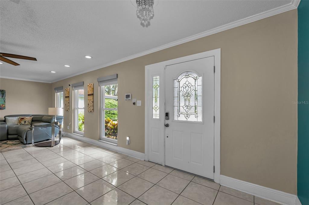 A bright entryway features light-colored tile flooring, a white front door, and adjacent living area — 1541 PLEASANT GROVE DRIVE, DUNEDIN, FL