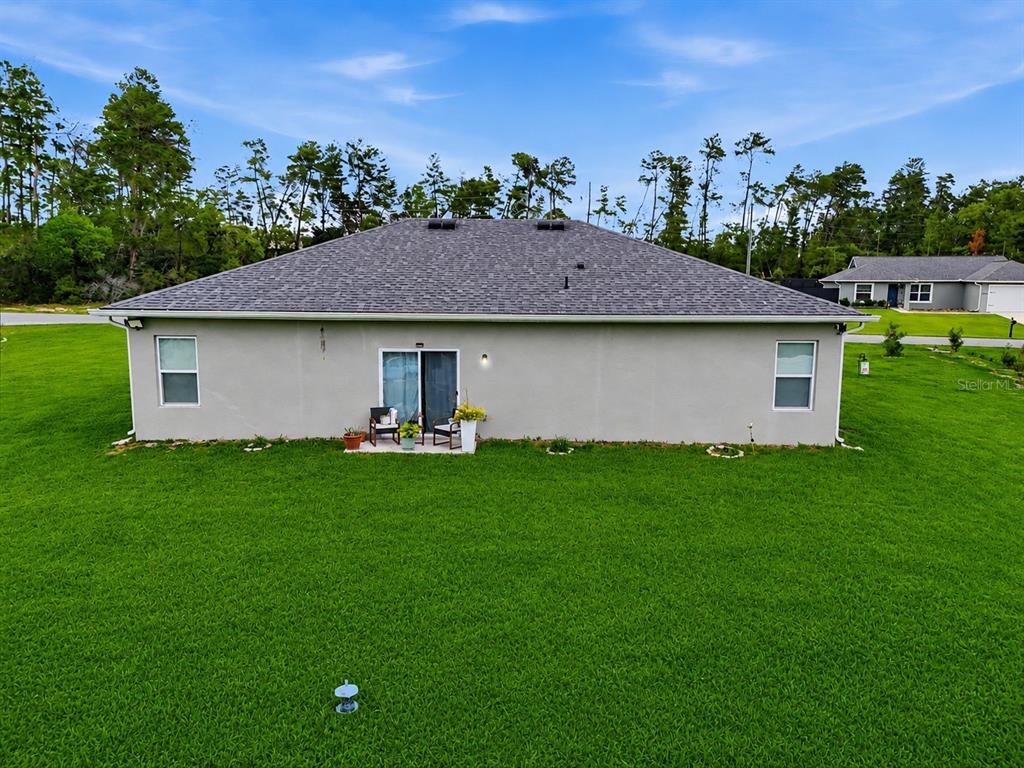 The rear exterior of a single-story house features a gray stucco facade and a patio — 15943 SW 53RD COURT, OCALA, FL