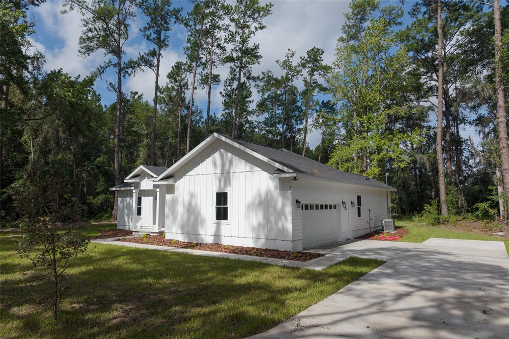A white farmhouse-style house with vertical siding and a concrete driveway sits among tall trees — 832 NW 5TH STREET, MICANOPY, FL
