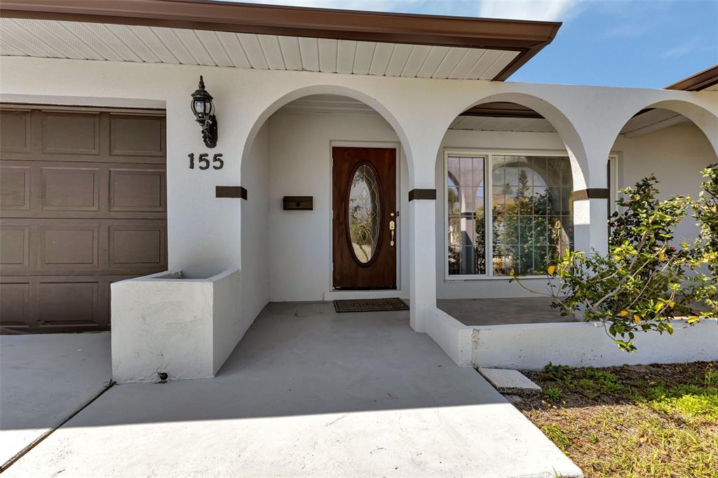 The exterior of a house features a white facade, arched entryways, and a brown door — 155 MORGAN LANE SE, PORT CHARLOTTE, FL