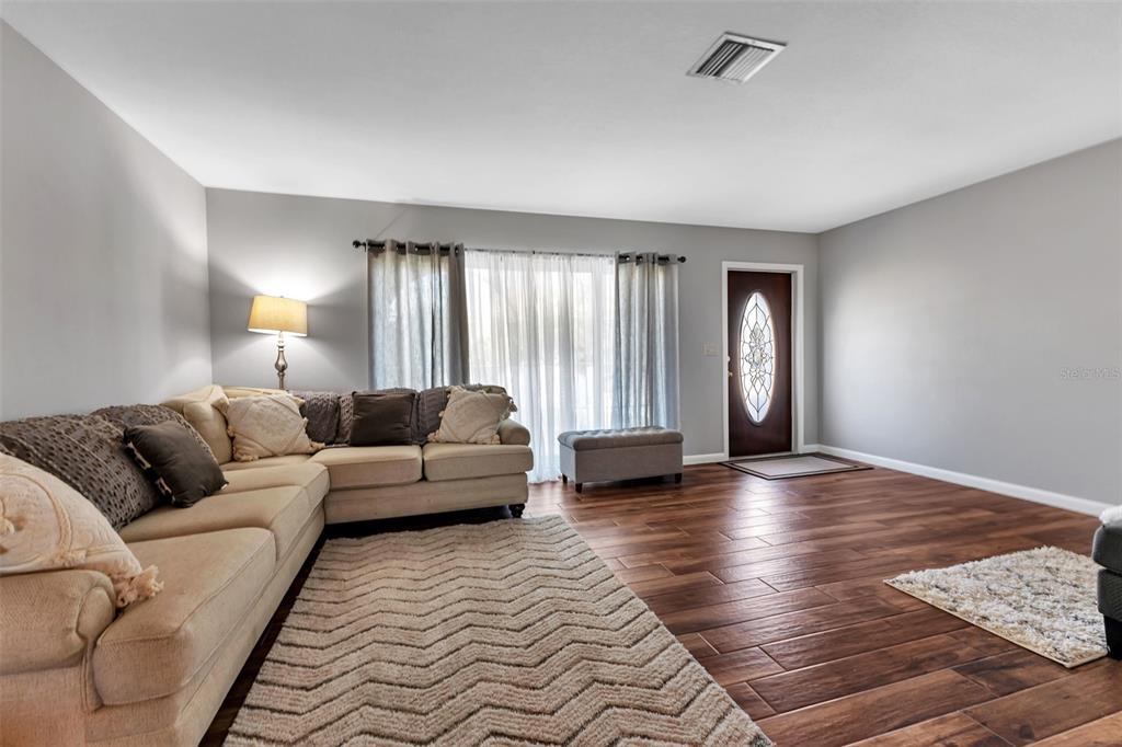 A living room features a beige sectional sofa, wood-look tile flooring, and a front door — 155 MORGAN LANE SE, PORT CHARLOTTE, FL