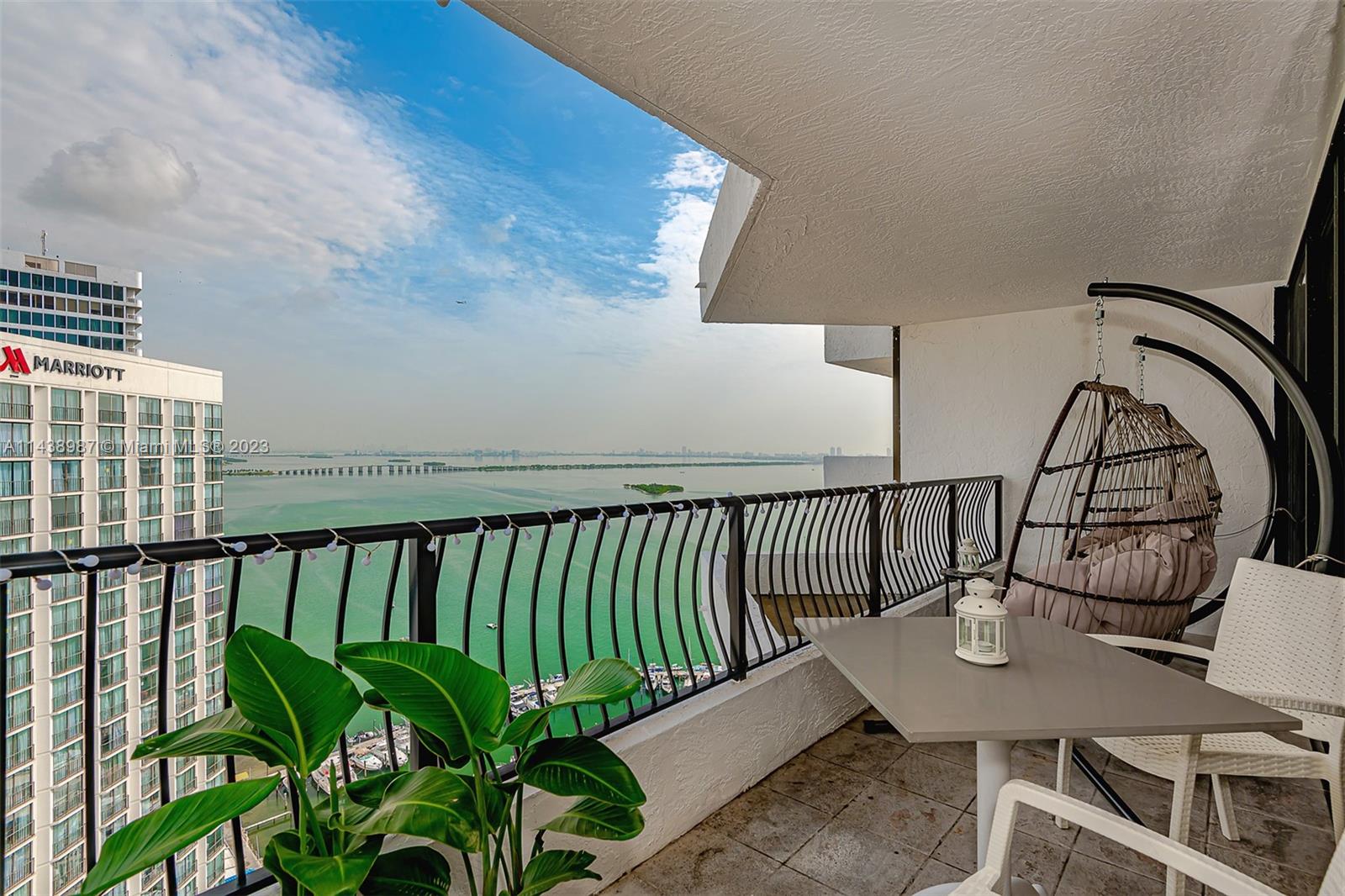 A balcony features a hanging chair, a small table, a plant, and a water view — 555 NE 15th St # 32E, Miami FL 33132, MIAMI, FL
