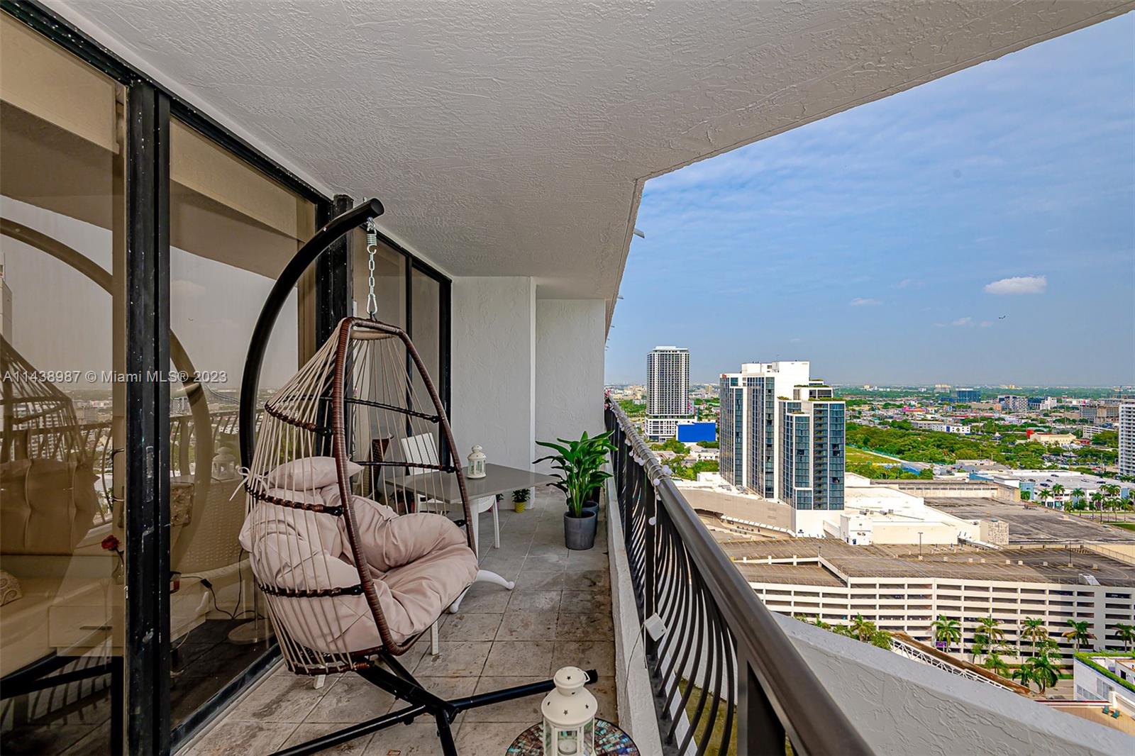 A balcony features a hanging egg chair, a small table, and a view of city buildings — 555 NE 15th St # 32E, Miami FL 33132, MIAMI, FL