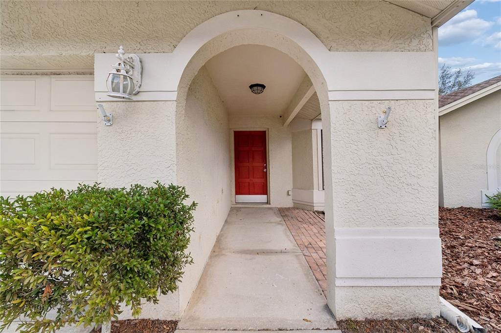 A covered entryway features a red front door, a concrete walkway, and a brick floor — 11903 STEPPINGSTONE BOULEVARD, TAMPA, FL