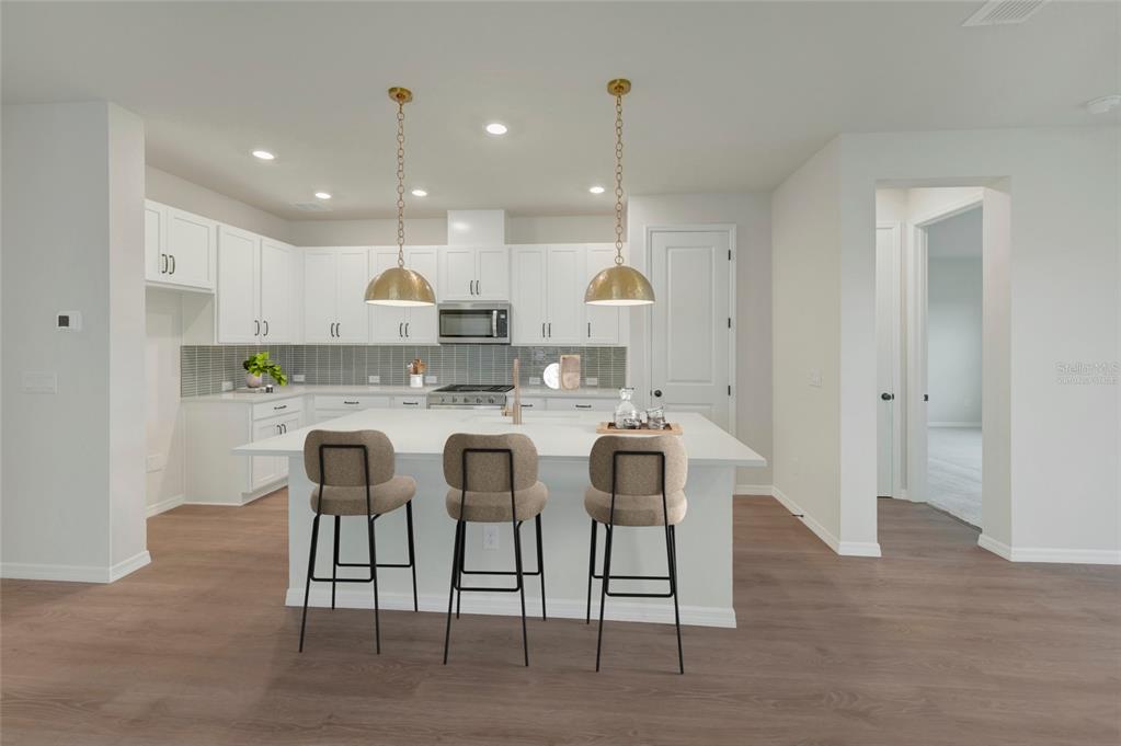 A modern kitchen features white cabinetry, a large island with three stools, and gold pendant lights — 5024 CHAPEL ROW AVENUE, APOLLO BEACH, FL