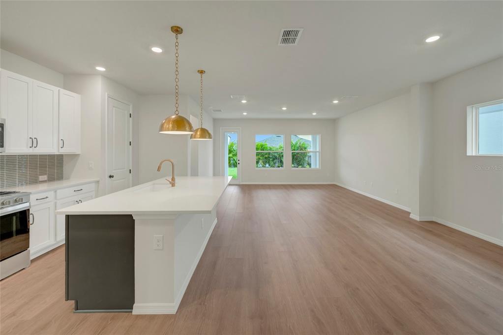 A modern kitchen with white cabinets and a large island opens into a spacious living area — 5024 CHAPEL ROW AVENUE, APOLLO BEACH, FL