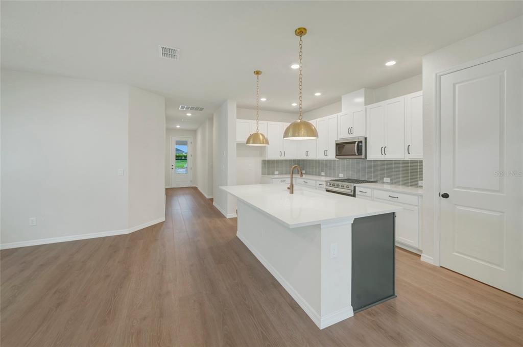 A modern kitchen features white cabinets, a large island with gold pendants, and wood flooring — 5024 CHAPEL ROW AVENUE, APOLLO BEACH, FL