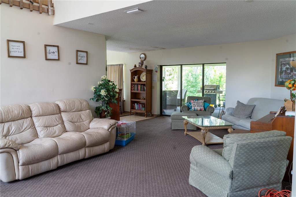 A carpeted living room features a beige sofa, armchairs, a glass coffee table, and a bookshelf — 4365 REAL COURT, ORLANDO, FL