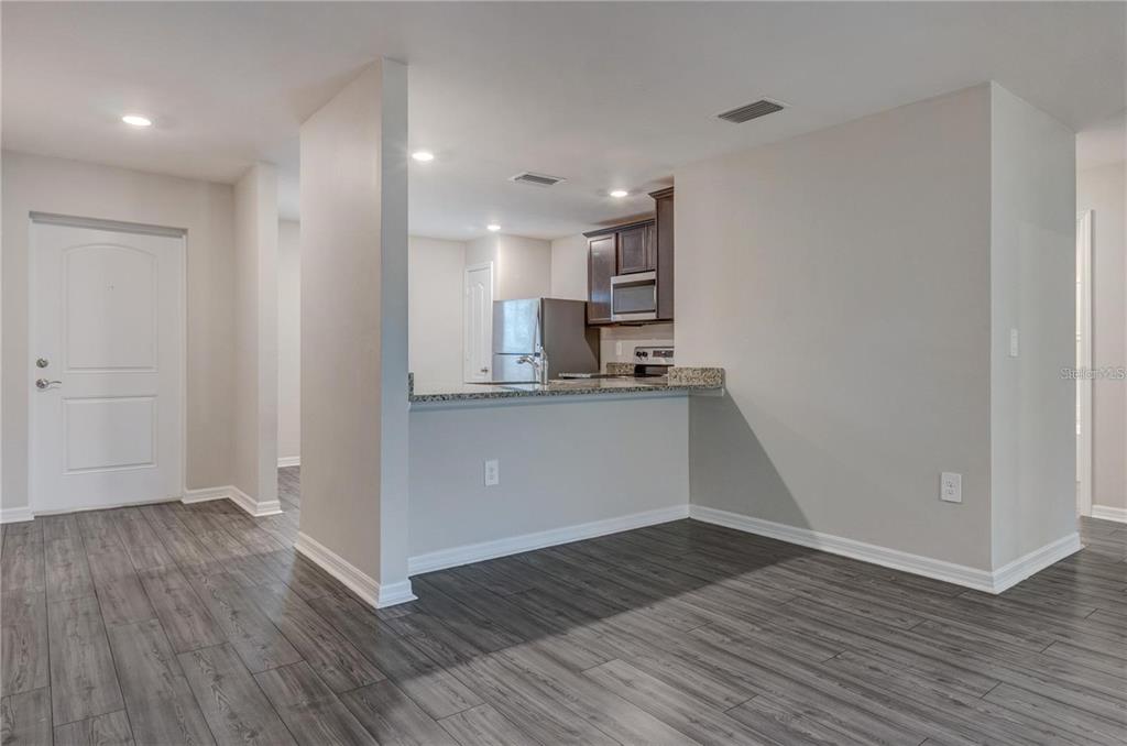 A kitchen with dark cabinets and granite countertops overlooks an open living area with flooring — 4127 SNOWDROP STREET, NORTH PORT, FL