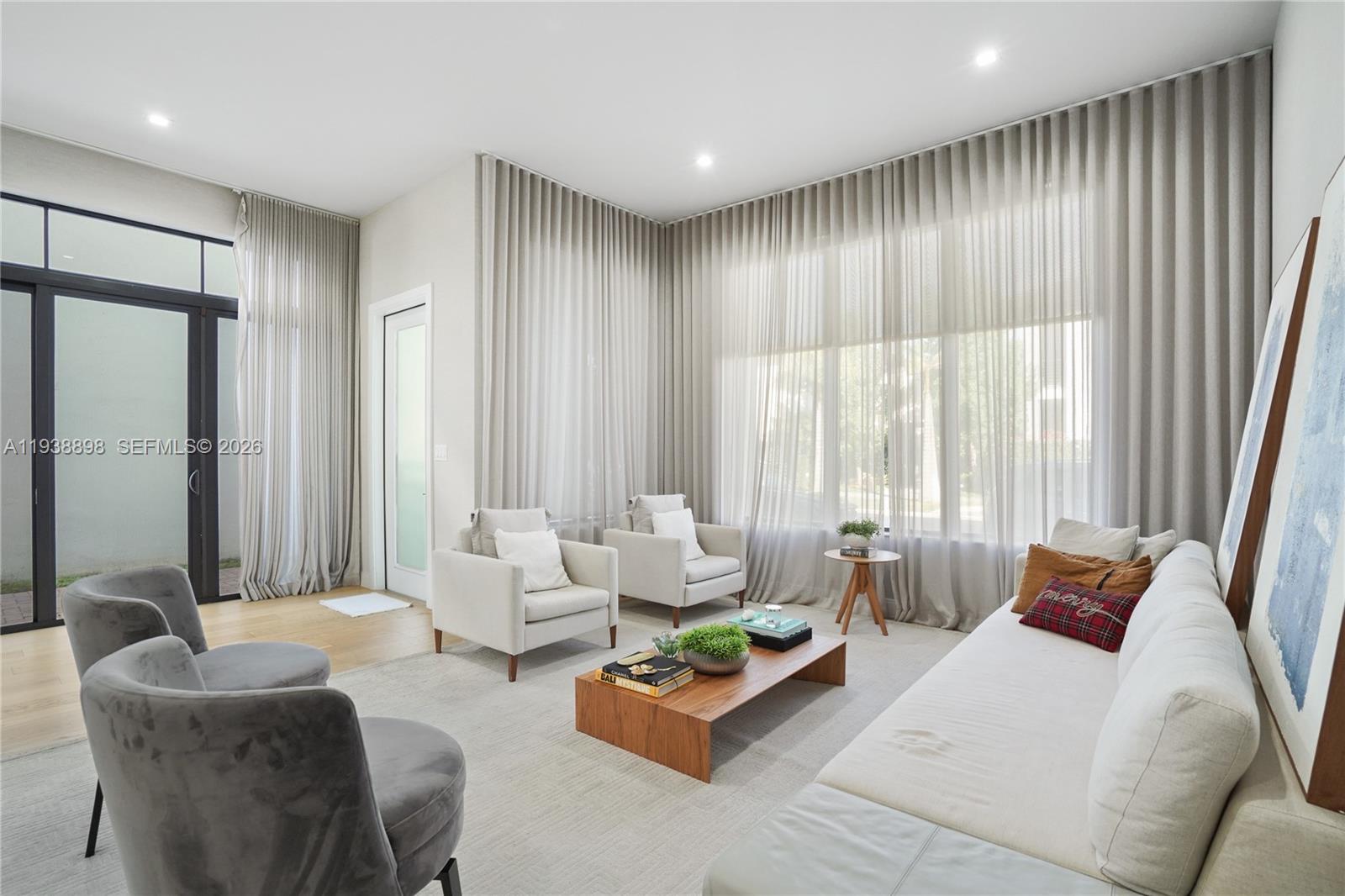 A modern living room features floor-to-ceiling curtains, a wooden coffee table, and neutral-toned seating — 8144 NW 43rd St, Doral FL 33166, DORAL, FL