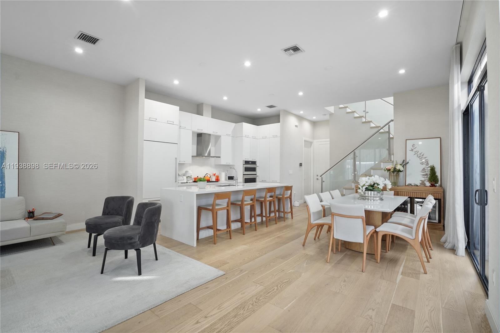 A modern open-concept kitchen and dining area features white cabinetry, a central island, and stairs — 8144 NW 43rd St, Doral FL 33166, DORAL, FL