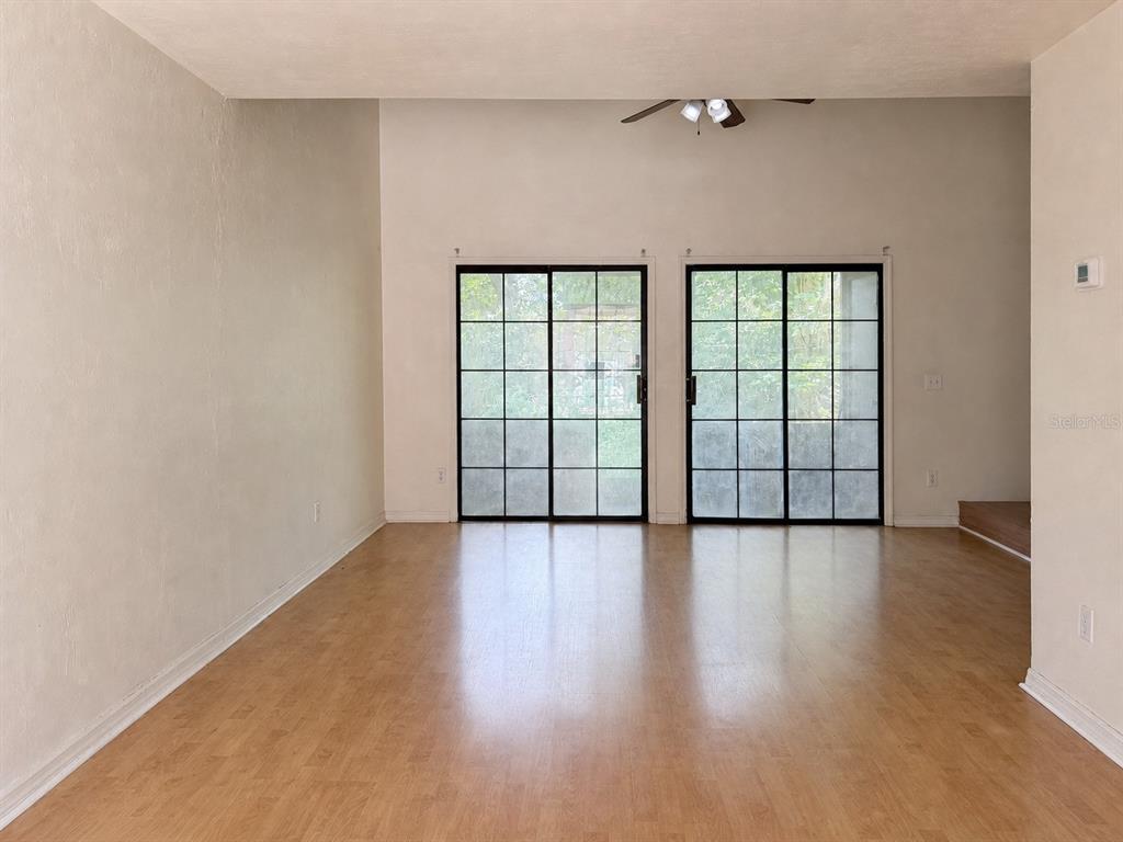 An empty room features light wood-look flooring, white walls, and two sets of glass sliding doors — 900 SW 62ND BOULEVARD UNIT G41, GAINESVILLE, FL