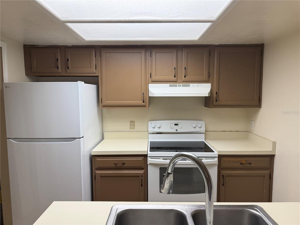 A kitchen features brown cabinets, white appliances, and a double sink in the foreground — 900 SW 62ND BOULEVARD UNIT G41, GAINESVILLE, FL