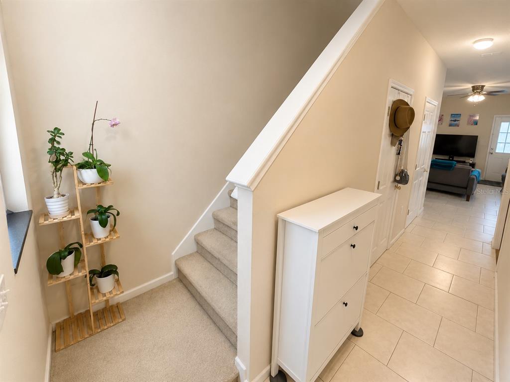 A staircase with a wooden plant stand sits beside a white cabinet in a hallway — 66 MOULTRIE VILLAGE LANE, ST AUGUSTINE, FL