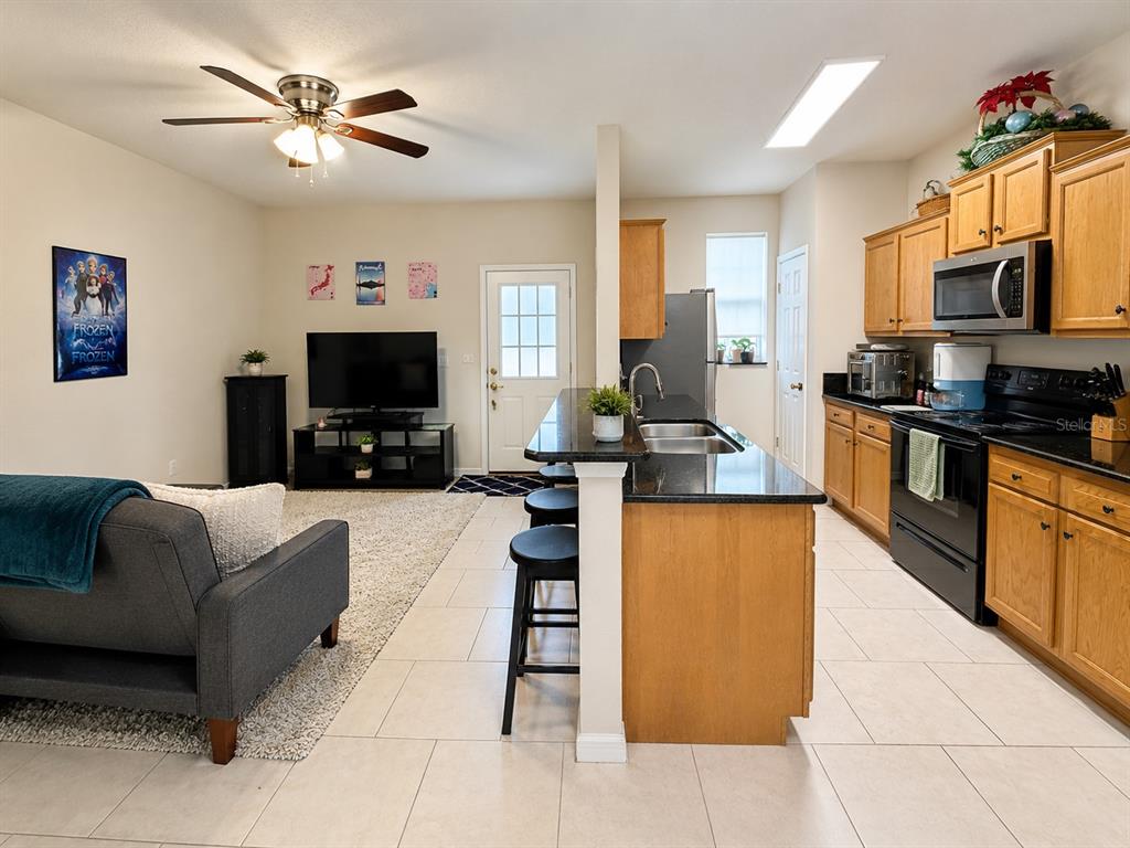 An open-concept living room and kitchen featuring a dark sofa, television, and wooden cabinetry — 66 MOULTRIE VILLAGE LANE, ST AUGUSTINE, FL