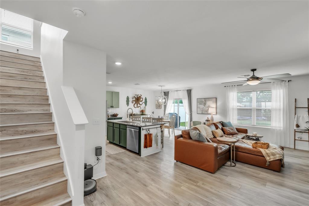 An open-concept living room and kitchen featuring light wood flooring, a brown sectional, and stairs — 4110 WILLOW HAMMOCK DR, PALMETTO, FL