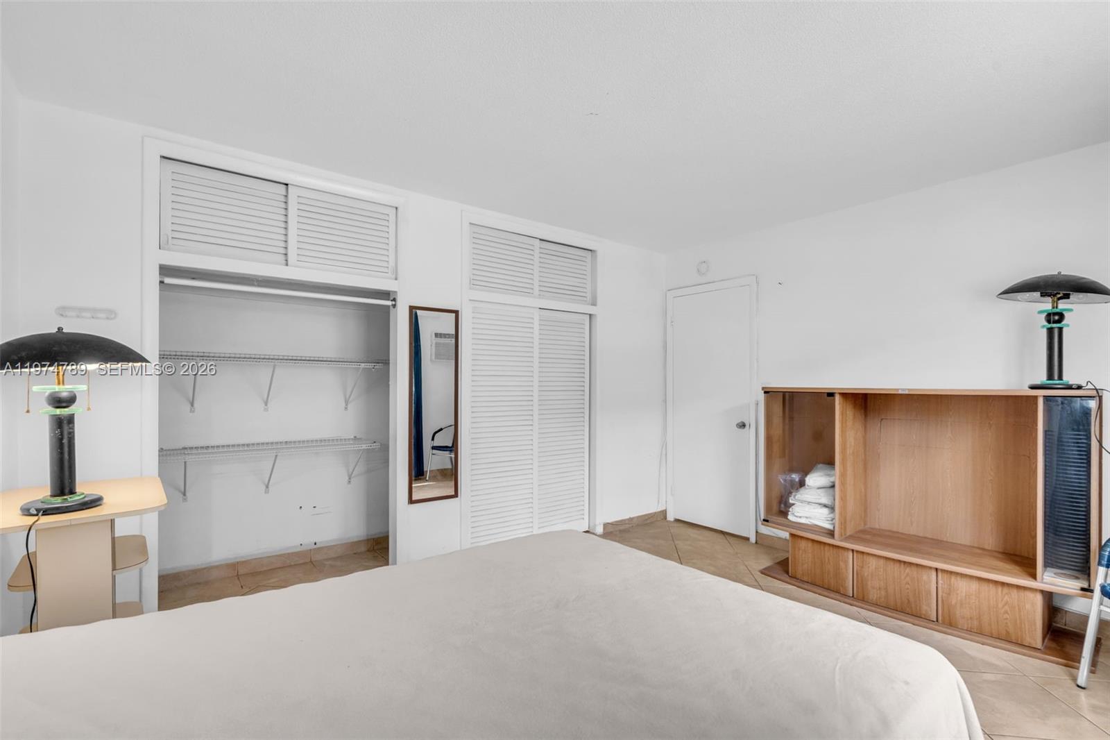 A bedroom features a bed, a built-in closet with louvered doors, and a wooden entertainment unit — 17050 NE 14th Ave # 106, Miami FL 33162, MIAMI, FL