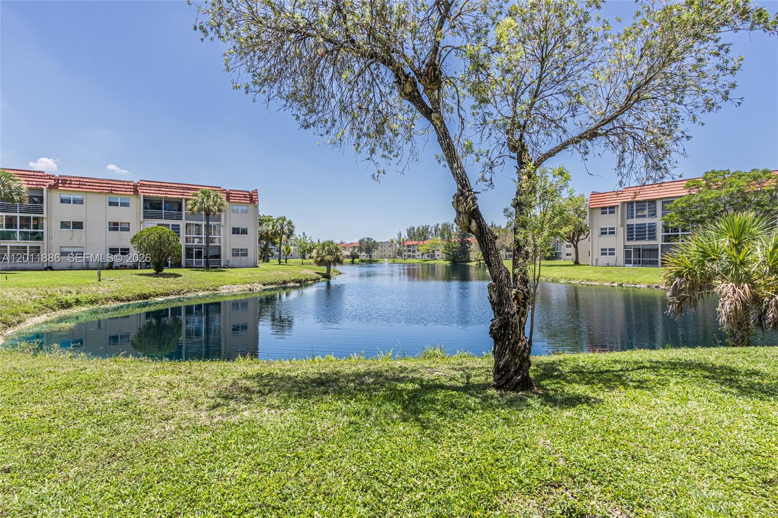 A pond sits between two multi-story apartment buildings with red-tiled roofs and green lawns — 2831 E Sunrise Lakes Dr # 105, Sunrise FL 33322, SUNRISE, FL