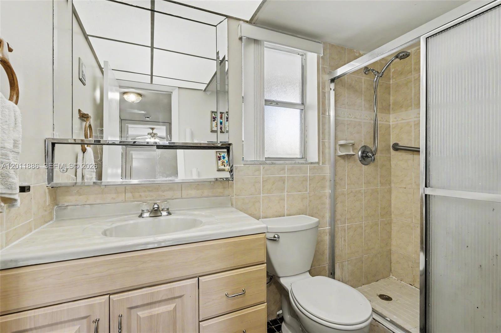 A bathroom features a light wood vanity, a toilet, and a tiled walk-in shower — 2831 E Sunrise Lakes Dr # 105, Sunrise FL 33322, SUNRISE, FL