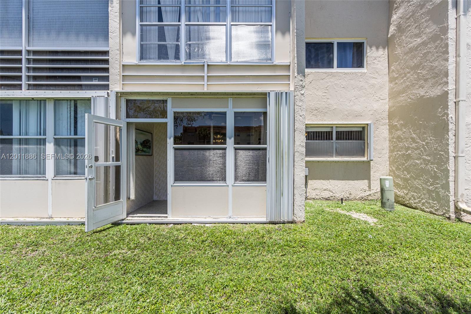 A ground-level patio with a screen door and windows sits beside a tan stucco building — 2831 E Sunrise Lakes Dr # 105, Sunrise FL 33322, SUNRISE, FL