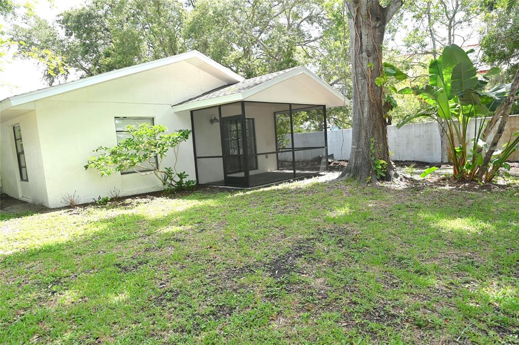 The exterior of a white house features a screened-in porch and a large backyard tree — 1976 DEBBIE STREET, SARASOTA, FL