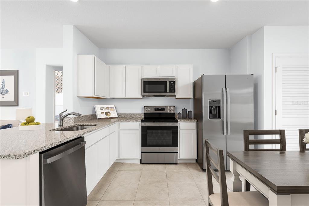A kitchen with white cabinets, granite countertops, stainless steel appliances, and tile flooring — 6932 SUNDIAL DRIVE, LAKELAND, FL