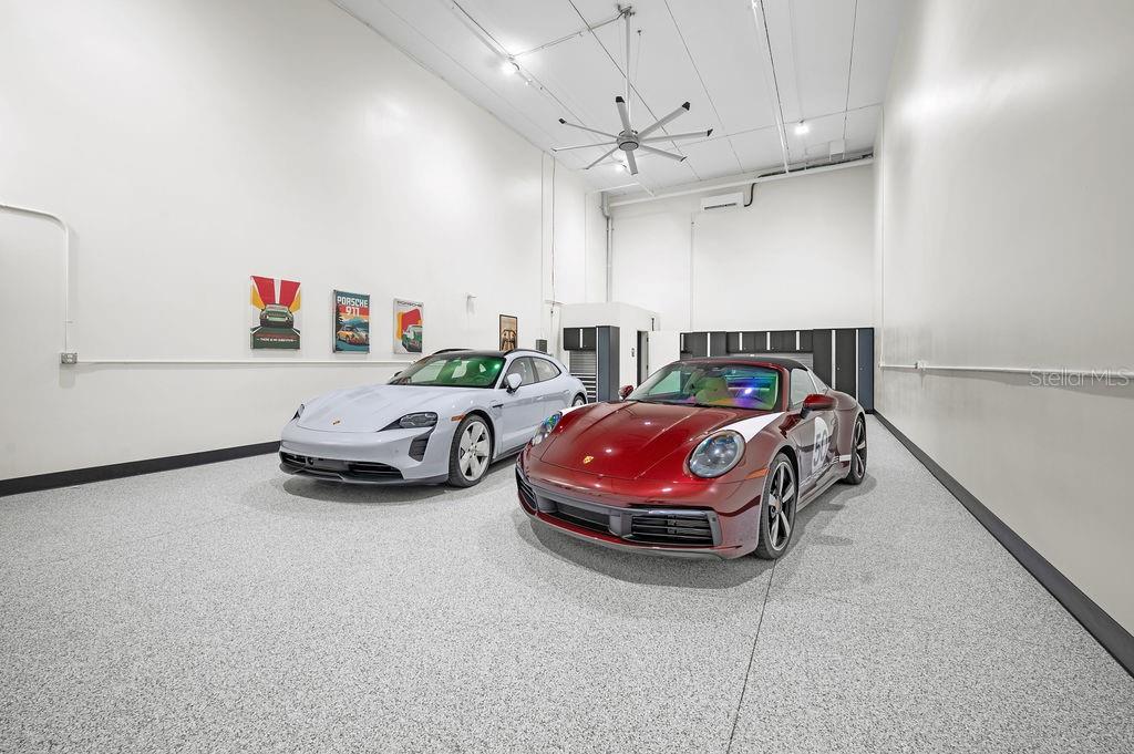 A spacious garage with epoxy flooring houses a silver Porsche Taycan and a red Porsche 911 — 5431 COMMUNICATIONS PARKWAY UNIT 29, LAKEWOOD RANCH, FL