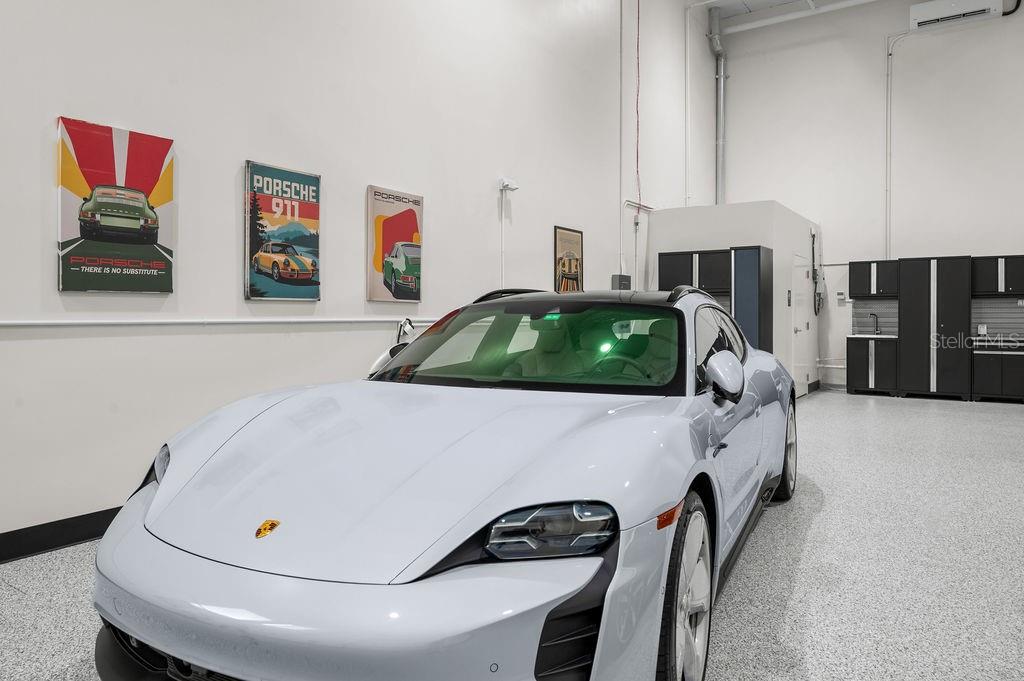 A light-colored Porsche Taycan is parked inside a garage with white walls and posters — 5431 COMMUNICATIONS PARKWAY UNIT 29, LAKEWOOD RANCH, FL