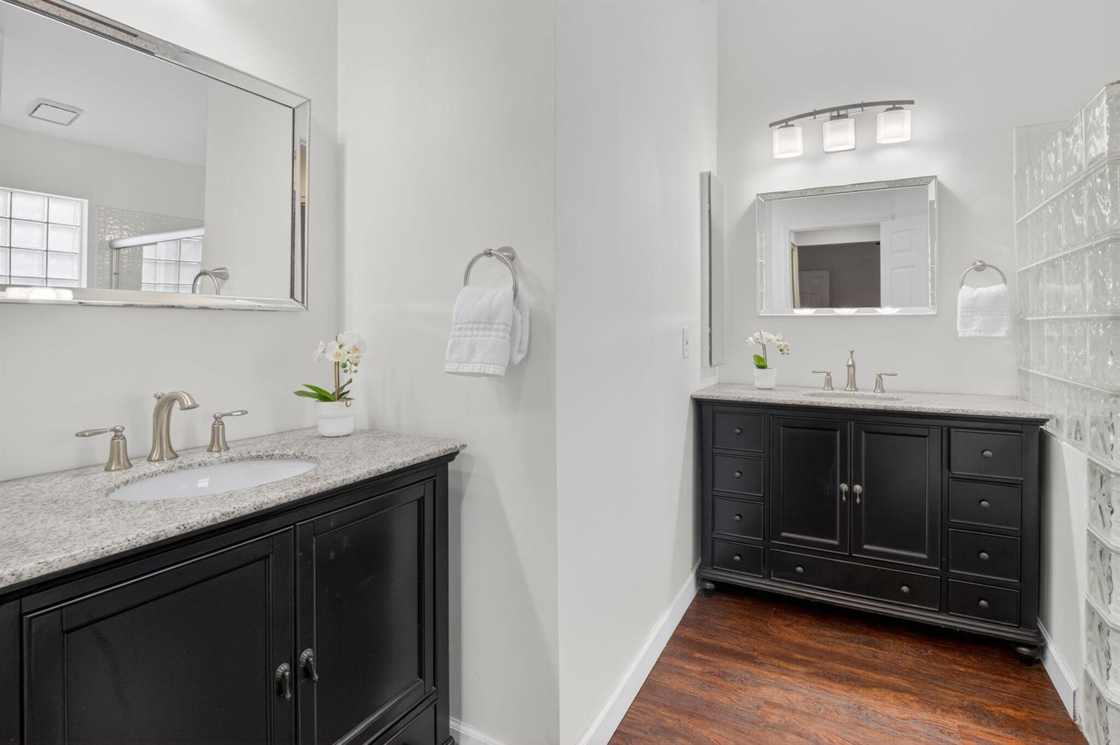 A bathroom features two black vanities with granite countertops, silver fixtures, and glass block walls — 7550 Ironbridge Circle, Delray Beach FL 33446, DELRAY BEACH, FL