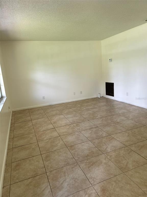 An empty room features light-colored walls, a textured ceiling, and tan square floor tiles — 2321 NE 39TH STREET, OCALA, FL