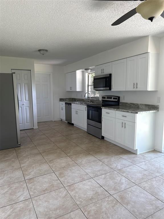 A kitchen features white cabinets, stainless steel appliances, granite countertops, and light-colored tile flooring — 2321 NE 39TH STREET, OCALA, FL