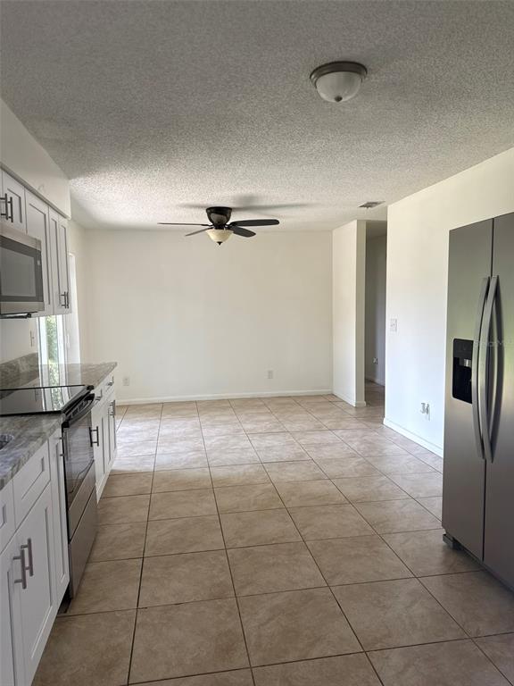 A kitchen with white cabinets, stainless steel appliances, and tile flooring opens to a dining area — 2321 NE 39TH STREET, OCALA, FL