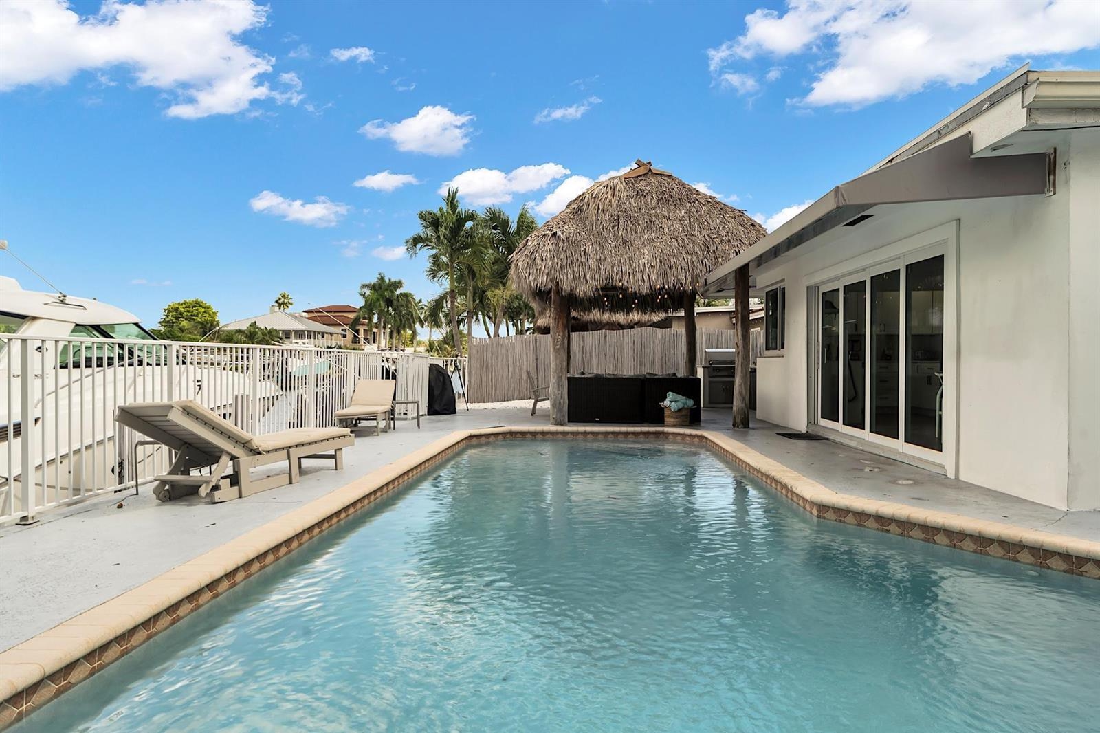 A swimming pool sits on a patio next to a house with a tiki hut — 2233 SE 15th Street, Pompano Beach FL 33062, POMPANO BEACH, FL